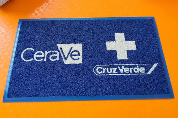 Tapete publicitario co-branding con logos de Caribe y Cruz Verde — regalo corporativo con marca compartida